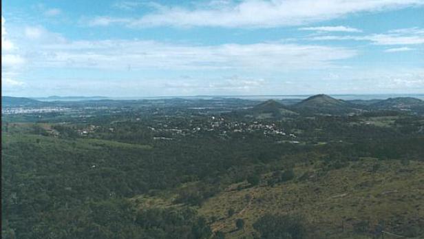 Eine weite Landschaft mit Hügeln, Wäldern und einer Stadt unter blauem Himmel.