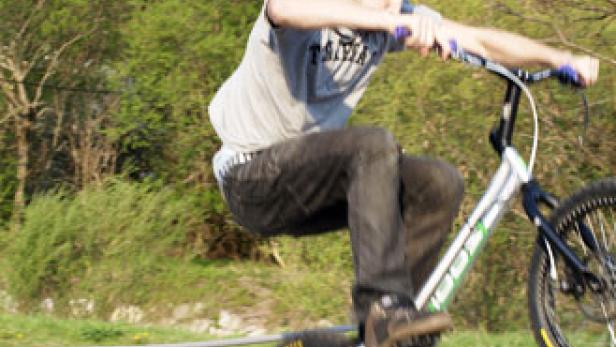 Ein junger Mann führt einen Trick mit seinem Trial-Bike im Freien aus.