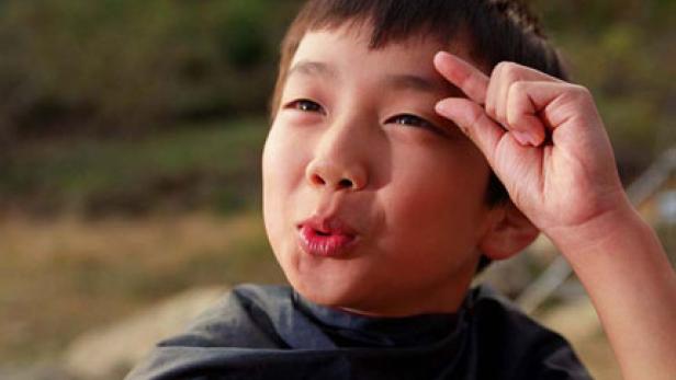 Ein Junge formt mit seinen Fingern eine kleine Geste vor seiner Stirn.