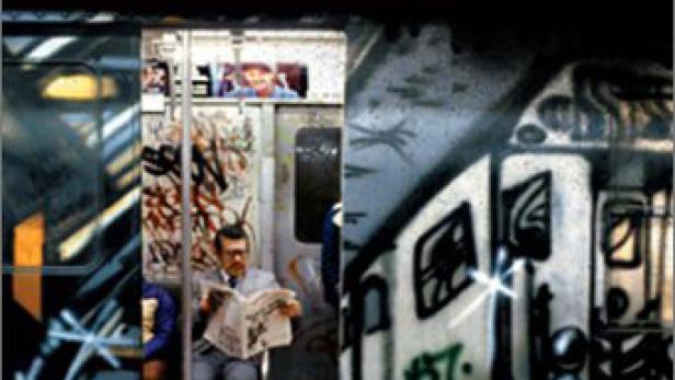 Ein Mann liest Zeitung in einer U-Bahn, deren Waggons mit Graffiti besprüht sind.
