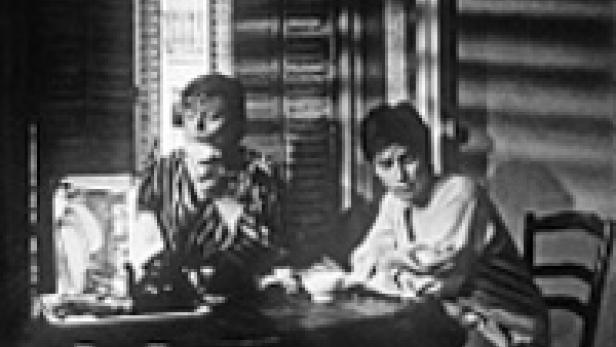 Zwei Frauen sitzen an einem Tisch in einem Raum mit starkem Schattenwurf.