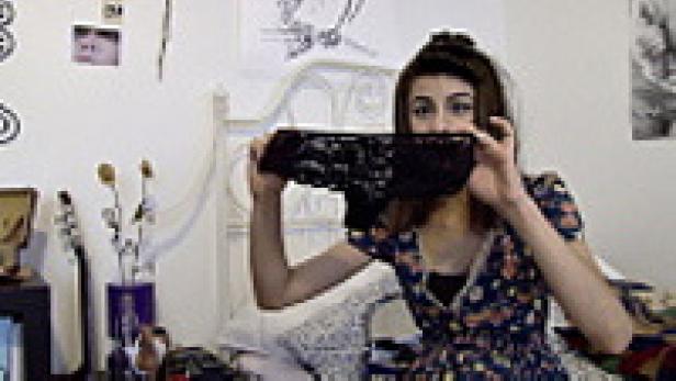 Eine junge Frau hält eine schwarze Spitzenunterhose vor ihr Gesicht.