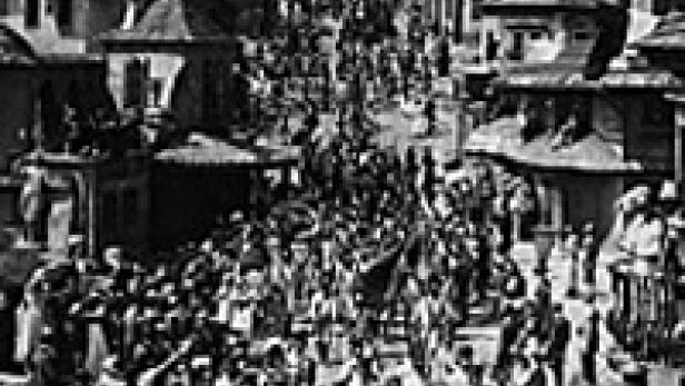 Eine Menschenmenge marschiert eine Straße in einer Stadt hinauf, im Hintergrund eine Kuppel.