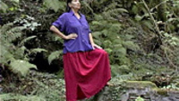 Eine Frau in einem blauen Hemd und einem roten Rock posiert in einem Wald.