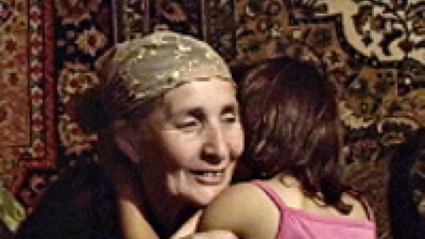 Eine ältere Frau mit Kopftuch umarmt ein junges Mädchen.