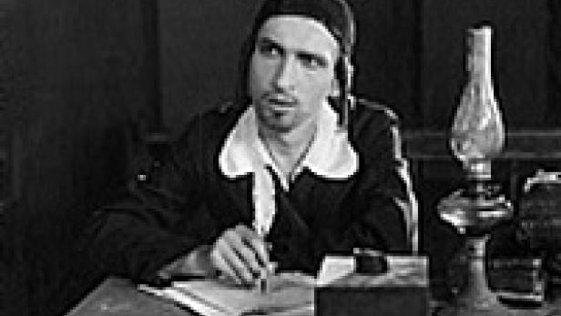 Ein Mann mit Mütze sitzt an einem Schreibtisch mit Feder und Tinte.