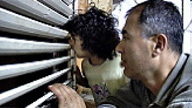 Ein Mann und ein Kind schauen durch eine Jalousie.