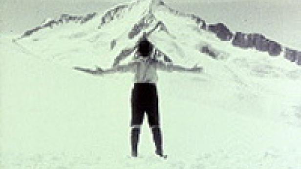 Eine Person steht mit ausgestreckten Armen vor einem schneebedeckten Berg.