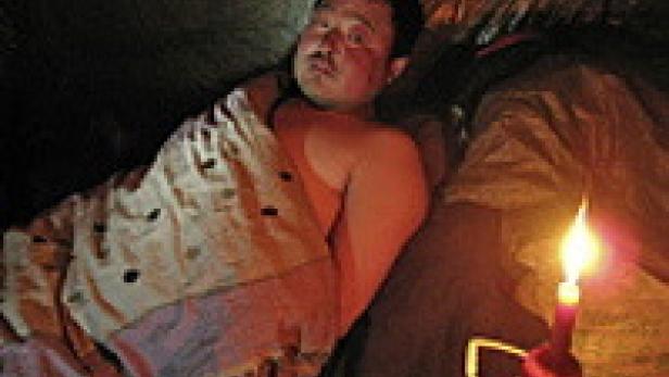 Ein Mann liegt in einer Decke gehüllt im Zelt, beleuchtet von einer Kerze.