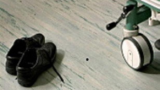 Ein Paar schwarze Schuhe steht neben einem Rollstuhlrad auf einem gemusterten Boden.