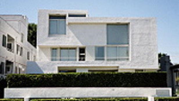 Ein modernes, weißes Haus mit großen Fenstern und einer grünen Hecke im Vorgarten.