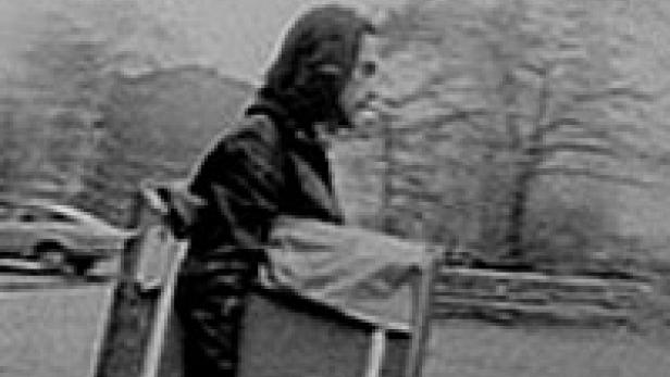 Eine Person mit Kapuze steht neben einem hölzernen Karren im Freien.