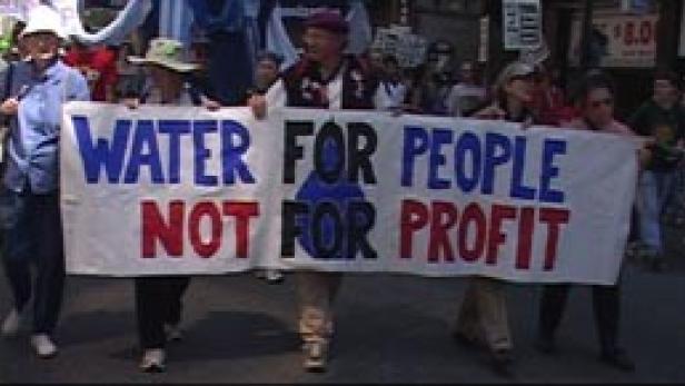 Mehrere Demonstranten halten ein Transparent mit der Aufschrift „Wasser für Menschen, nicht für Profit“.
