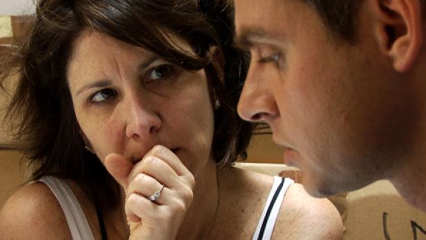 Eine Frau mit einem Ring am Finger wirkt besorgt, während ein Mann neben ihr aufmerksam zuhört.