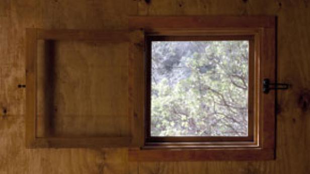 Ein kleines, hölzernes Fenster ist teilweise geöffnet und gibt den Blick auf Bäume frei.