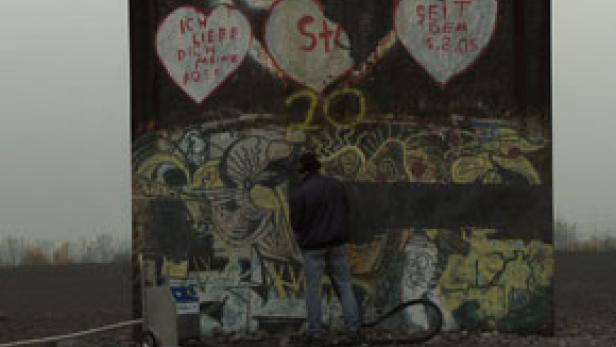 Eine Person reinigt Graffiti von einem Teil der Berliner Mauer.