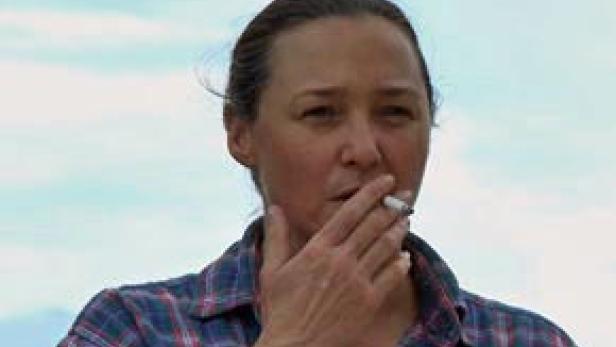 Eine Frau mit kariertem Hemd raucht eine Zigarette.