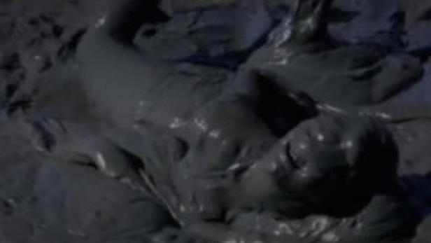 Eine Person liegt vollständig mit Schlamm bedeckt im Schlamm.