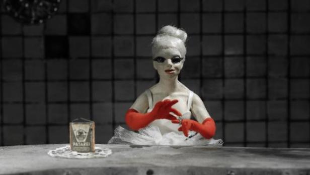 Eine Puppe mit roten Handschuhen und weißem Tutu sitzt an einem Tisch.