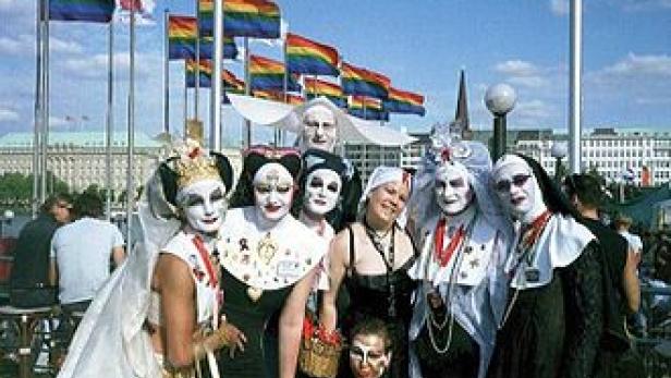 Eine Gruppe von Menschen, einige als Nonnen verkleidet, posiert vor Regenbogenflaggen.