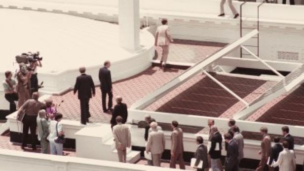 Eine Gruppe von Menschen steht auf einer Dachterrasse mit Ziegelboden.