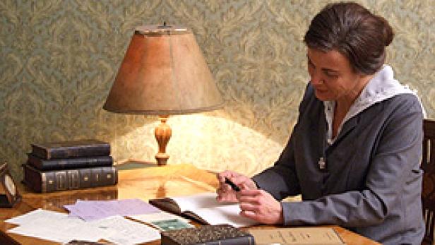 Eine Frau sitzt an einem Schreibtisch und schreibt in ein Buch.