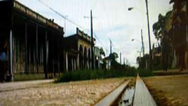 Eine Straße mit alten Gebäuden und Bahngleisen in einer ländlichen Gegend.