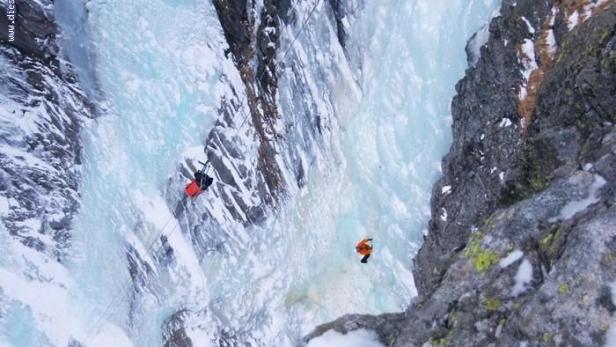 Zwei Personen überqueren eine eisige Schlucht mit einer Seilrutsche.
