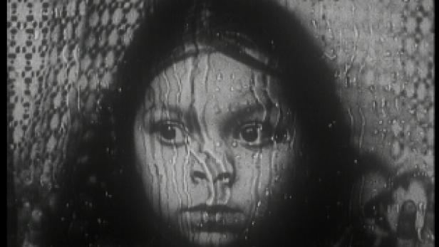 Das Gesicht eines Mädchens ist durch eine regennasse Fensterscheibe zu sehen.