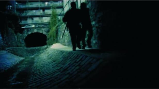 Zwei dunkle Silhouetten gehen nachts an einem Bach entlang.