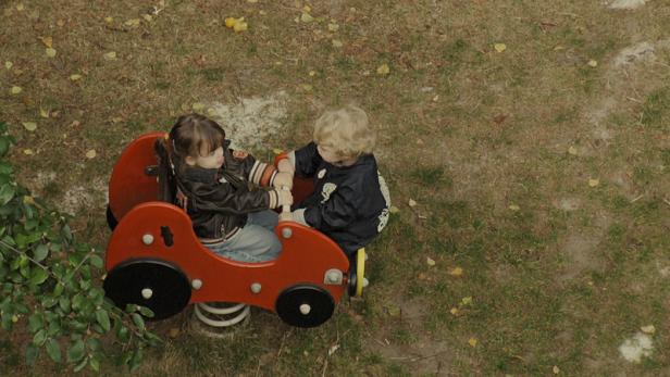 Zwei Kinder spielen auf einem roten Schaukeltier in Form eines Autos.