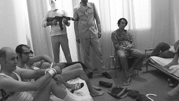 Geiseln sind gefesselt, während Bewaffnete in einem Raum stehen.