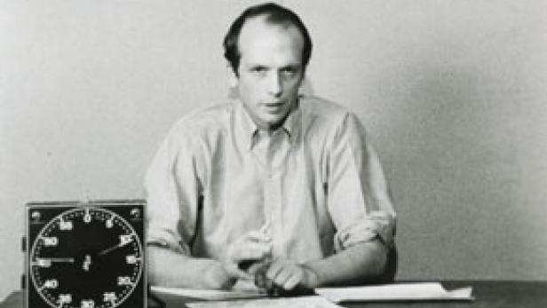 Ein Mann sitzt an einem Tisch mit einer großen Uhr und Papieren.