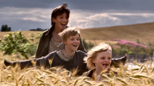 Drei lachende Jungen rennen durch ein goldenes Weizenfeld.