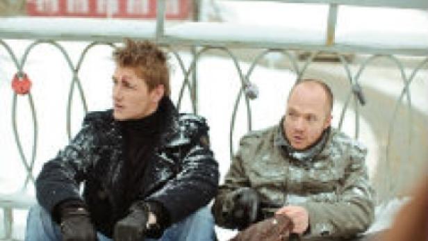 Zwei Männer sitzen im Winter auf einer Brücke mit Liebesschlössern.