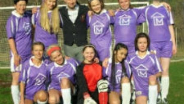 Eine Mädchenfußballmannschaft posiert mit ihrem Trainer für ein Gruppenfoto.