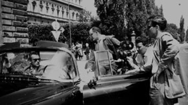 Ein Filmteam dreht eine Szene mit einem Auto auf einer Straße.