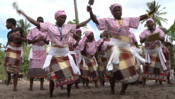 Eine Gruppe Frauen in traditioneller Kleidung tanzt am Strand.