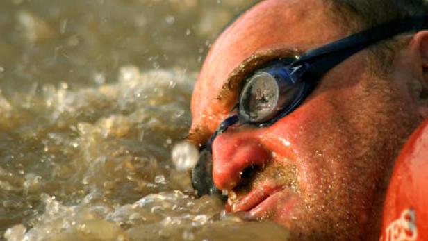 Ein Mann mit Schwimmbrille schwimmt im trüben Wasser.