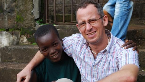 Ein lächelnder Mann mit Brille umarmt einen Jungen auf einer Treppe.