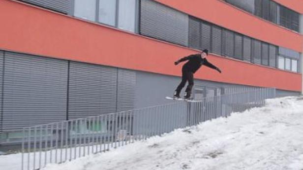 Ein Snowboarder springt über eine Rampe vor einem orangefarbenen Gebäude.