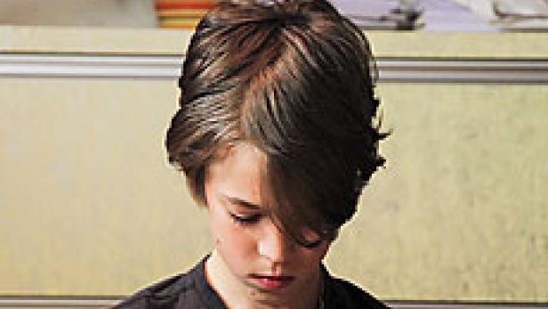 Ein junger Mensch mit braunen Haaren blickt nach unten.