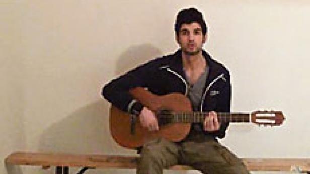 Ein junger Mann sitzt auf einer Bank und spielt Gitarre.