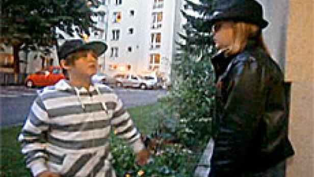 Ein Junge und ein Mädchen unterhalten sich vor einem Wohnhaus.