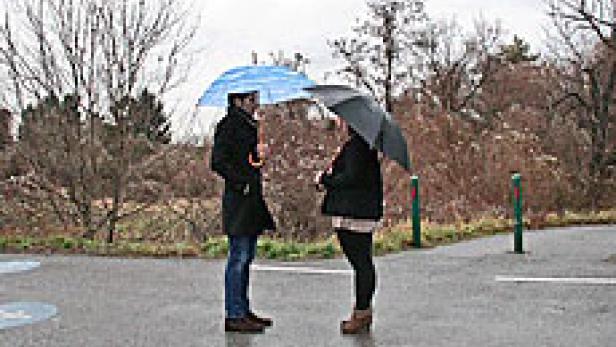Zwei Personen stehen mit Regenschirmen im Regen und unterhalten sich.
