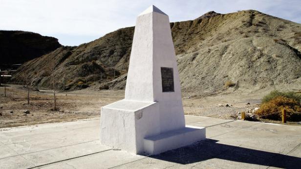 Ein weißes Denkmal steht vor einer kargen Hügellandschaft.