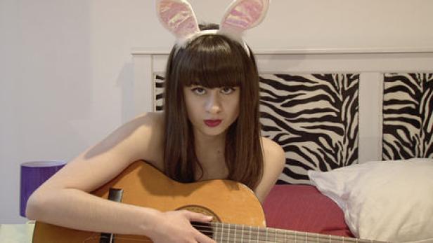 Eine junge Frau mit Hasenohren spielt Gitarre im Bett.