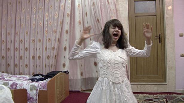 Eine junge Frau im Hochzeitskleid schreit mit erhobenen Händen.