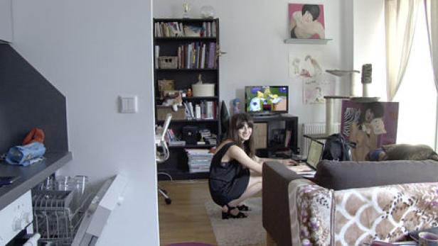Eine Frau hockt in einem Wohnzimmer und benutzt einen Laptop.