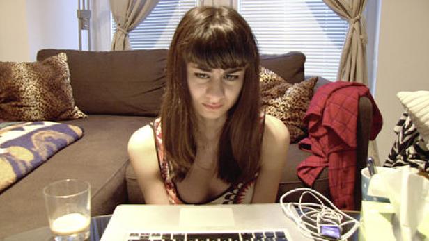 Eine junge Frau sitzt vor einem Laptop und schaut besorgt auf den Bildschirm.